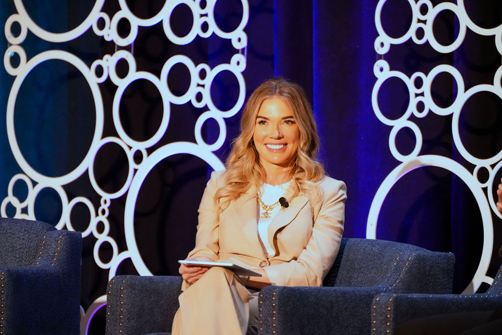 Heidi Arndt smiling while seated onstage during a conference conversation